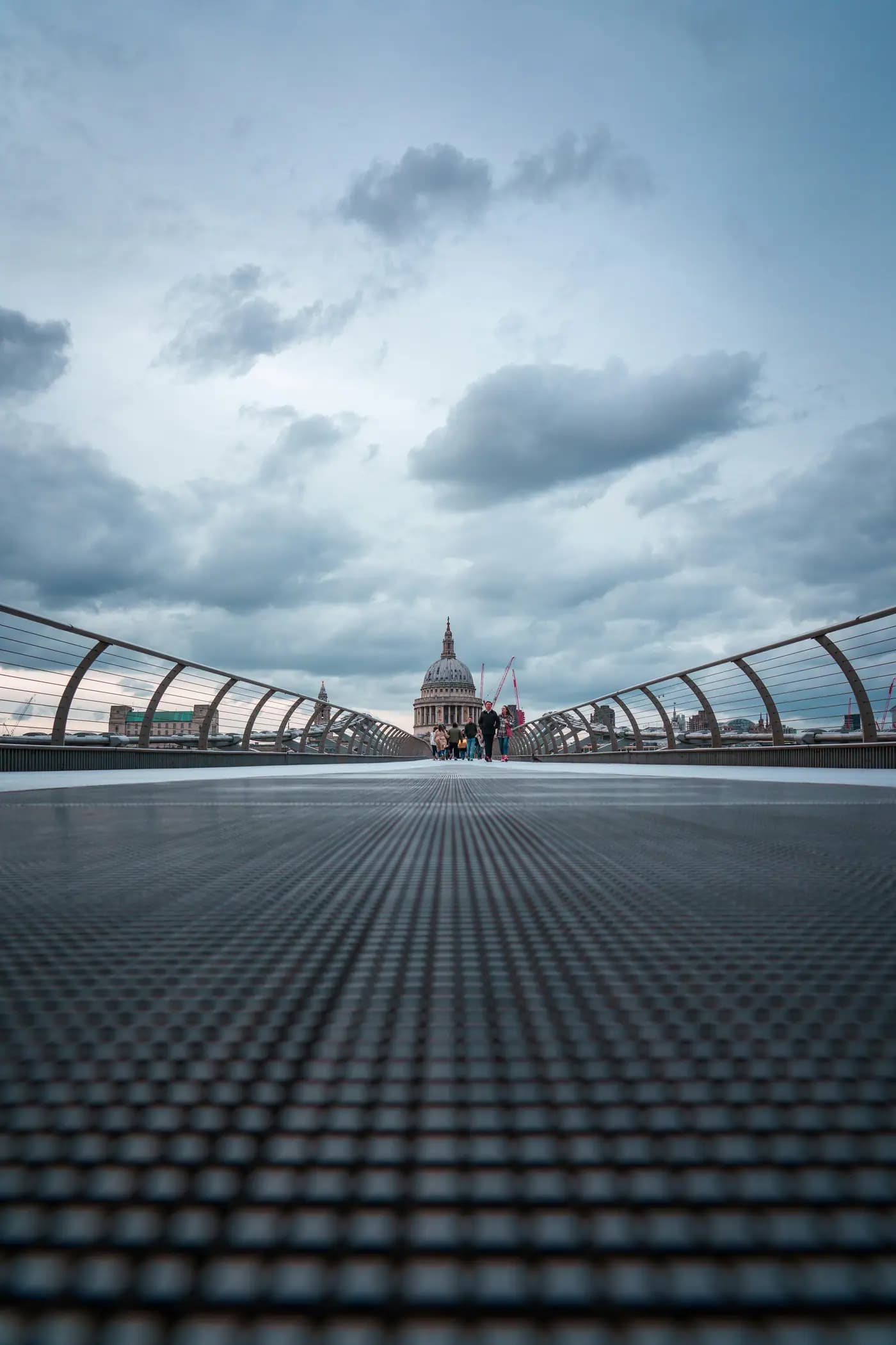 Perspective shot of pedestrians crossing a modern bridge toward a dome.